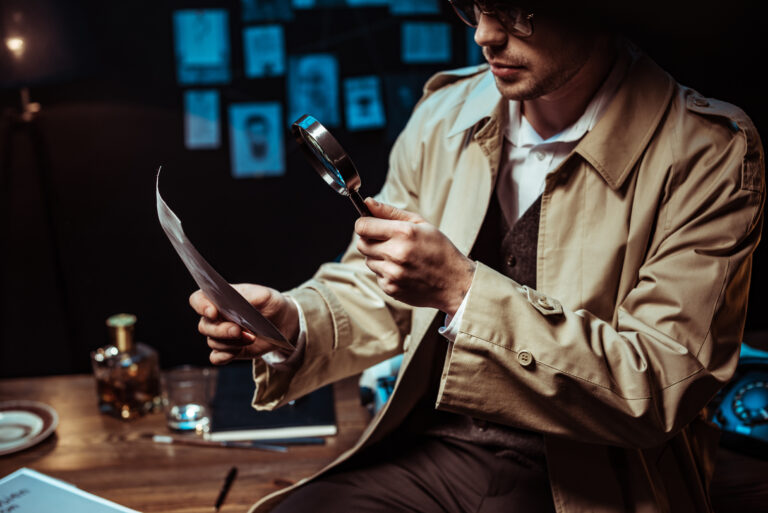 Cropped view of detective in trench coat looking at photo through magnifier