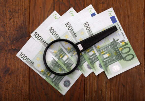 Top view of a magnifier on cash Euro bills on a wooden surface